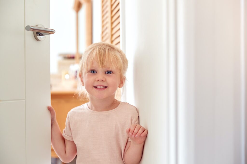 Portrait Of Young Girl Opening And Looking Around Door At Home
